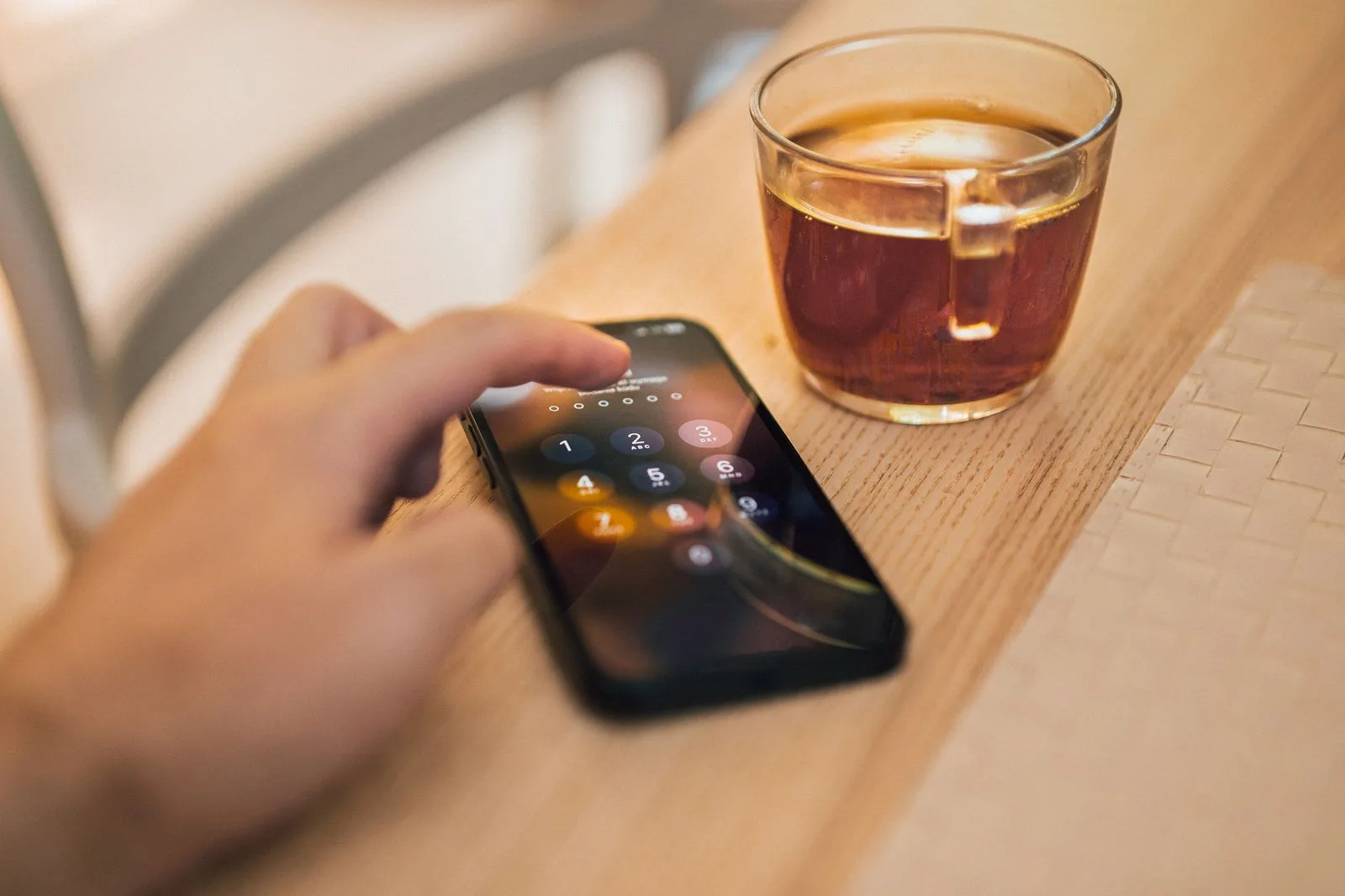 Une main déverrouille un smartphone posé sur une table en bois, à côté d'une tasse de thé
